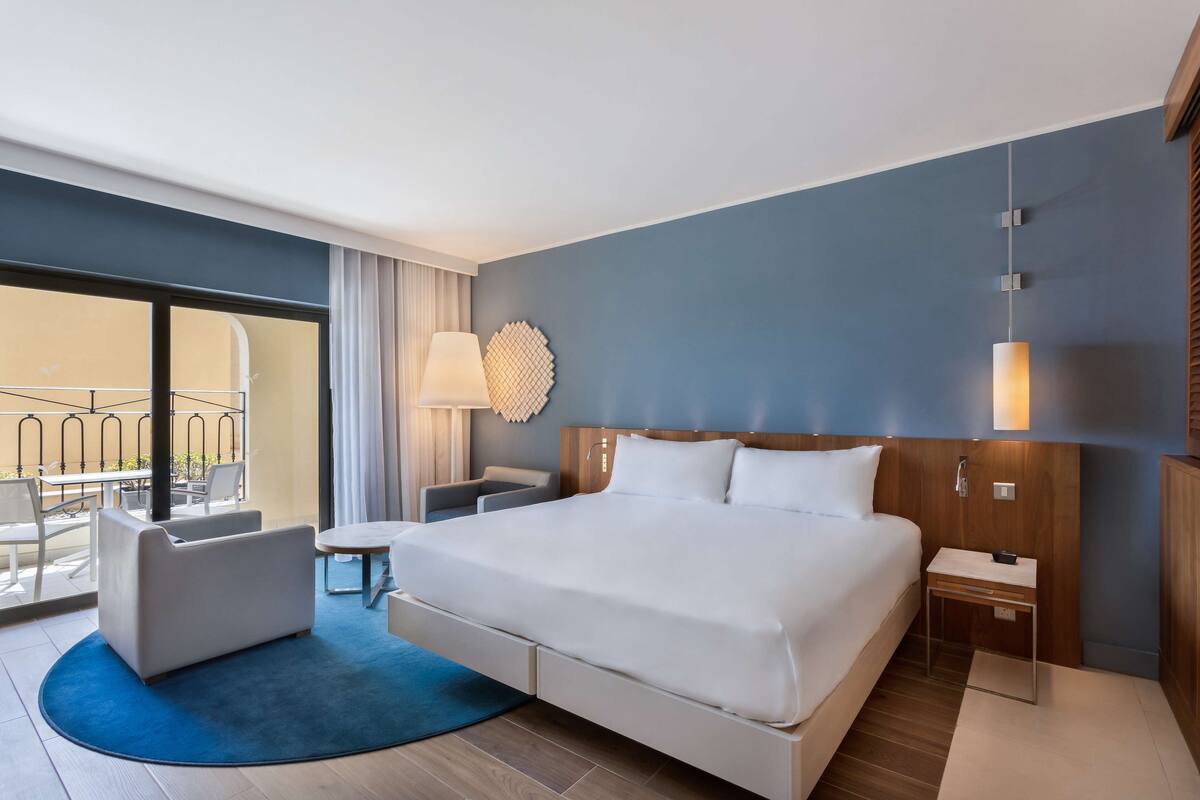 Une chambre d’hôtel moderne dotée d’un grand lit, d’un bureau, d’une chaise et d’un balcon avec coin salon extérieur.