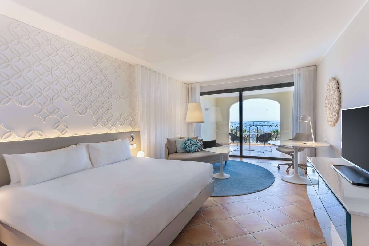 Une chambre d’hôtel avec un grand lit, un coin salon avec une table, une télévision et une vue sur l’extérieur.