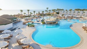 A resort pool area with multiple swimming pools, sun loungers, umbrellas, and a view of the ocean. - Safir Sharm Waterfalls Resort (Sharm El Sheikh)