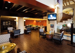 A spacious lobby with a wooden floor, seating arrangements, a television, and a staircase.