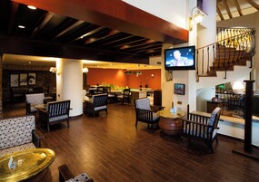 A spacious lobby with a wooden floor, seating arrangements, a television, and a staircase.