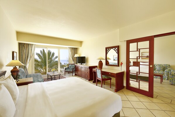 A hotel room with a large bed, a desk with a chair, a television, and a view of palm trees through the window. - Safir Sharm Waterfalls Resort (Sharm El Sheikh)