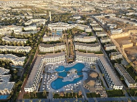 An aerial view of a resort with multiple buildings, a central pool area, and surrounding greenery.