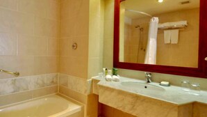 A bathroom with a bathtub, a shower, a sink with toiletries, and a large mirror.