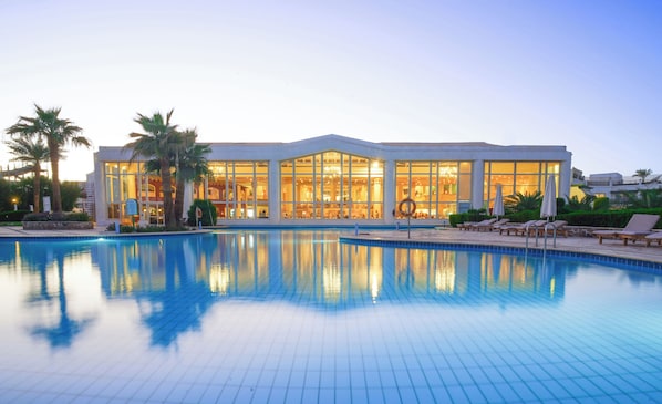 A hotel with a swimming pool, large windows, and palm trees.