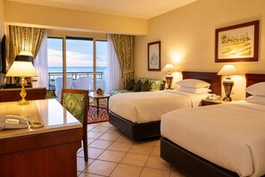 A hotel room with two beds, a desk with a telephone, a chair, a small table with fruit, and a balcony with a view. - Safir Sharm Waterfalls Resort (Sharm El Sheikh)