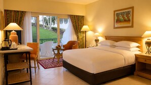 A hotel room with a bed, a desk, a chair, a small table with fruit, and a painting on the wall. - Safir Sharm Waterfalls Resort (Sharm El Sheikh)