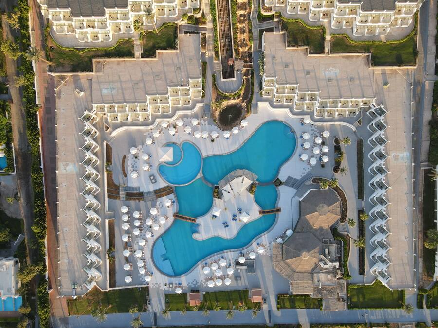 Vista aérea de un hotel con una piscina central grande, múltiples piscinas y un jardín bien cuidado.