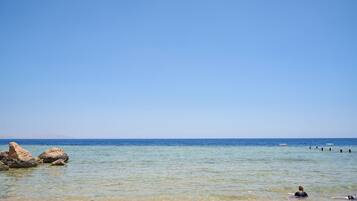 Ein Strand mit klarem Wasser, Felsen und einer Person, die schwimmt.