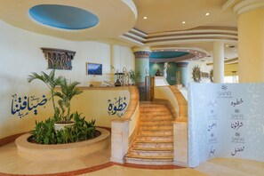 A grand lobby with a marble staircase, decorative columns, and a reception desk with multilingual signage. - Safir Sharm Waterfalls Resort (Sharm El Sheikh)