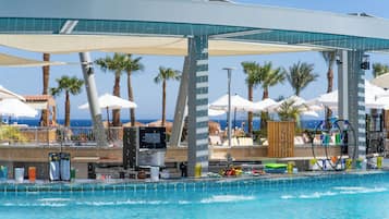 Zona de piscina con bar, sombrillas y palmeras.