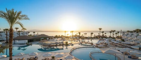 Un resort con múltiples piscinas, tumbonas y sombrillas, rodeado de palmeras y vistas al mar.