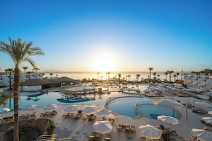 A resort with multiple swimming pools, sun loungers, and umbrellas, surrounded by palm trees and overlooking the sea.