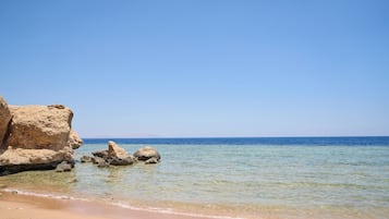 A beach with clear water, sandy shore, and rocky formations.