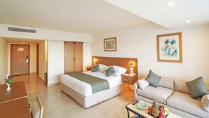 A hotel room with a bed, a sofa, a coffee table, and a desk with a vase of flowers.