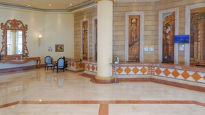 A lobby with a reception desk, two chairs, a large column, and a wall with ancient Egyptian-style artwork. - Safir Sharm Waterfalls Resort (Sharm El Sheikh)