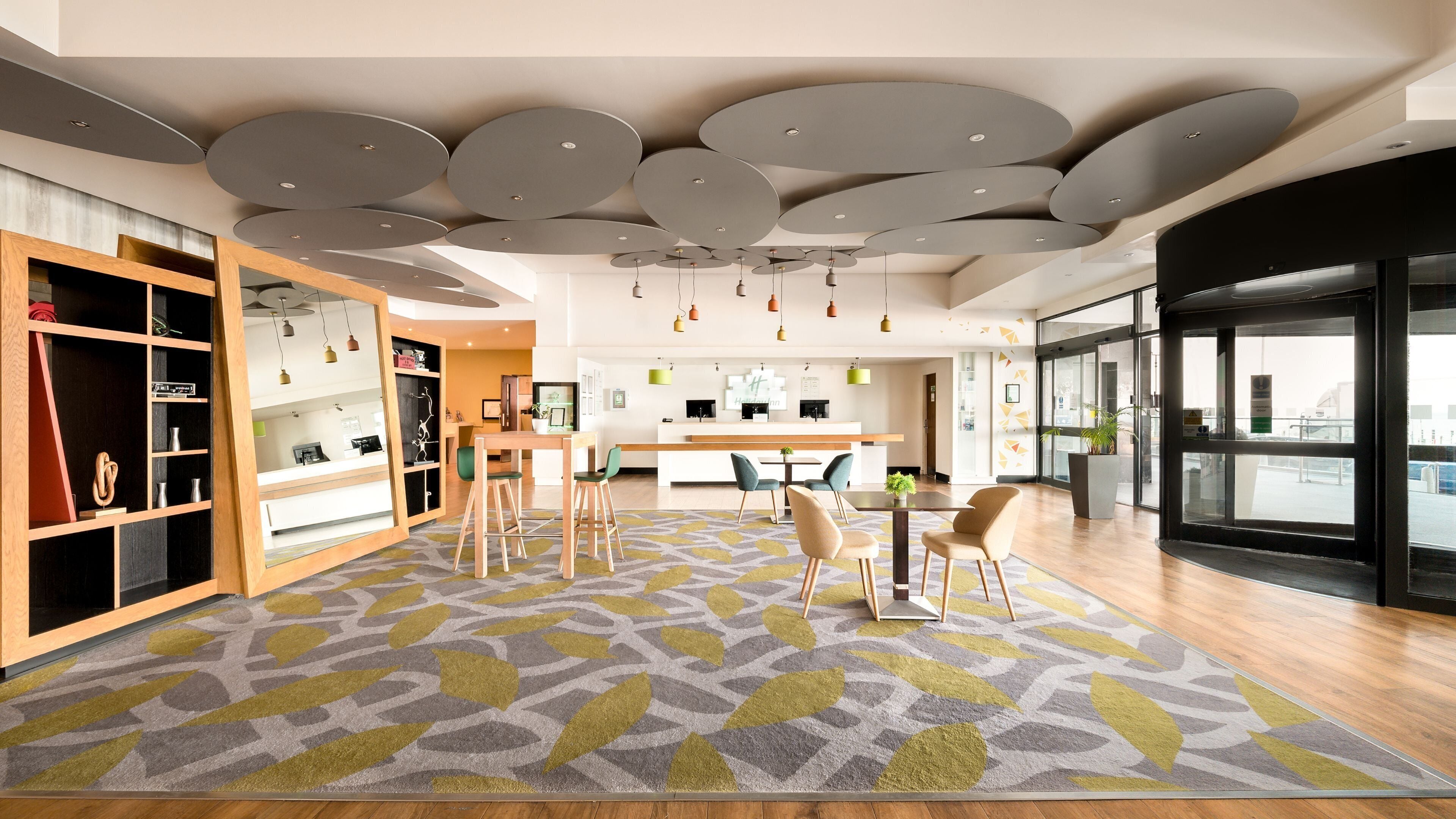 A modern interior with a central dining area, a reception desk, and a large window offering a view.