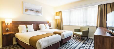 A hotel room with two beds, a desk, a chair, a TV, and a window with curtains.