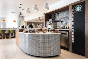 A modern coffee shop interior with a central counter, seating area, and a Starbucks sign. - Holiday Inn Brighton Seafront by IHG (Brighton)