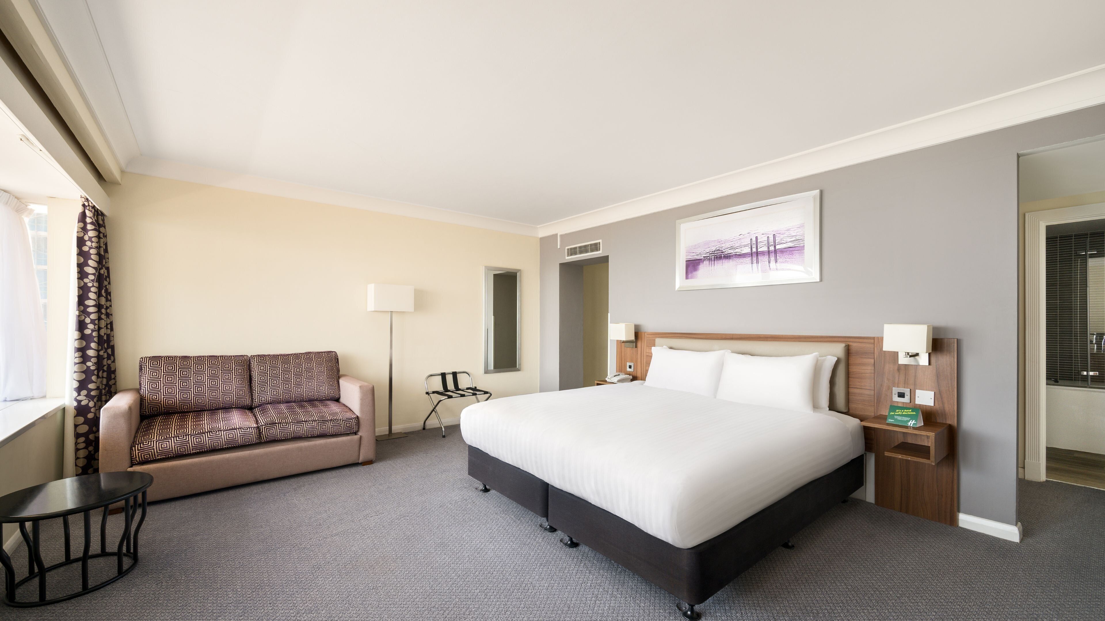 Habitació d'hotel amb un llit gran, un sofà, un escriptori i una làmpada.