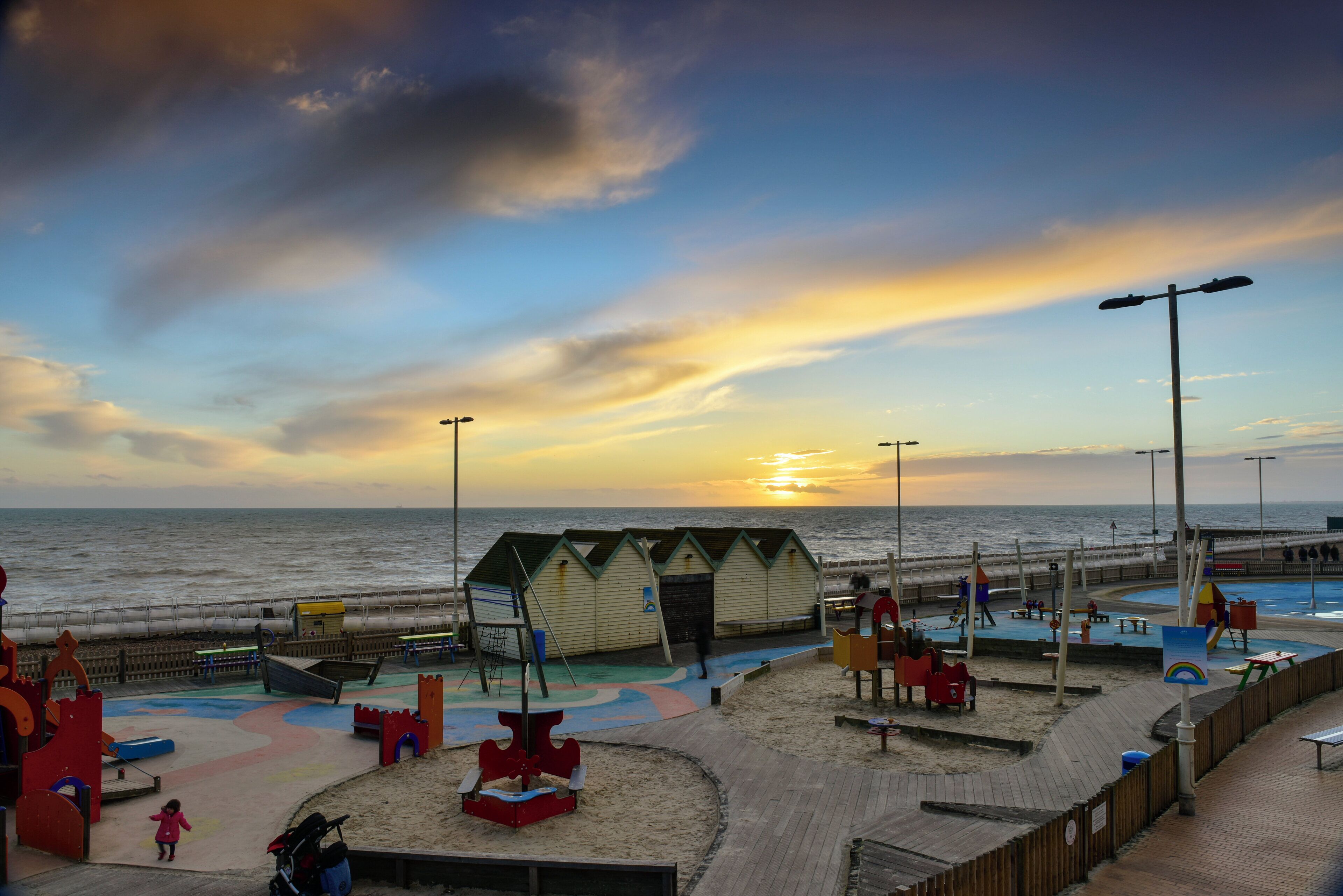 Un parque infantil en la playa con zonas de juego en arena y una estructura de madera.