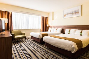 Two single beds with wooden headboards, a flat-screen TV, and a seating area with a chair and table.