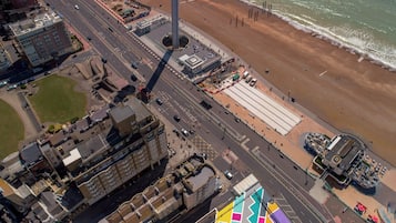 An aerial view of a coastal city with a prominent tower, a colorful building with geometric patterns, and a beach with a pier.