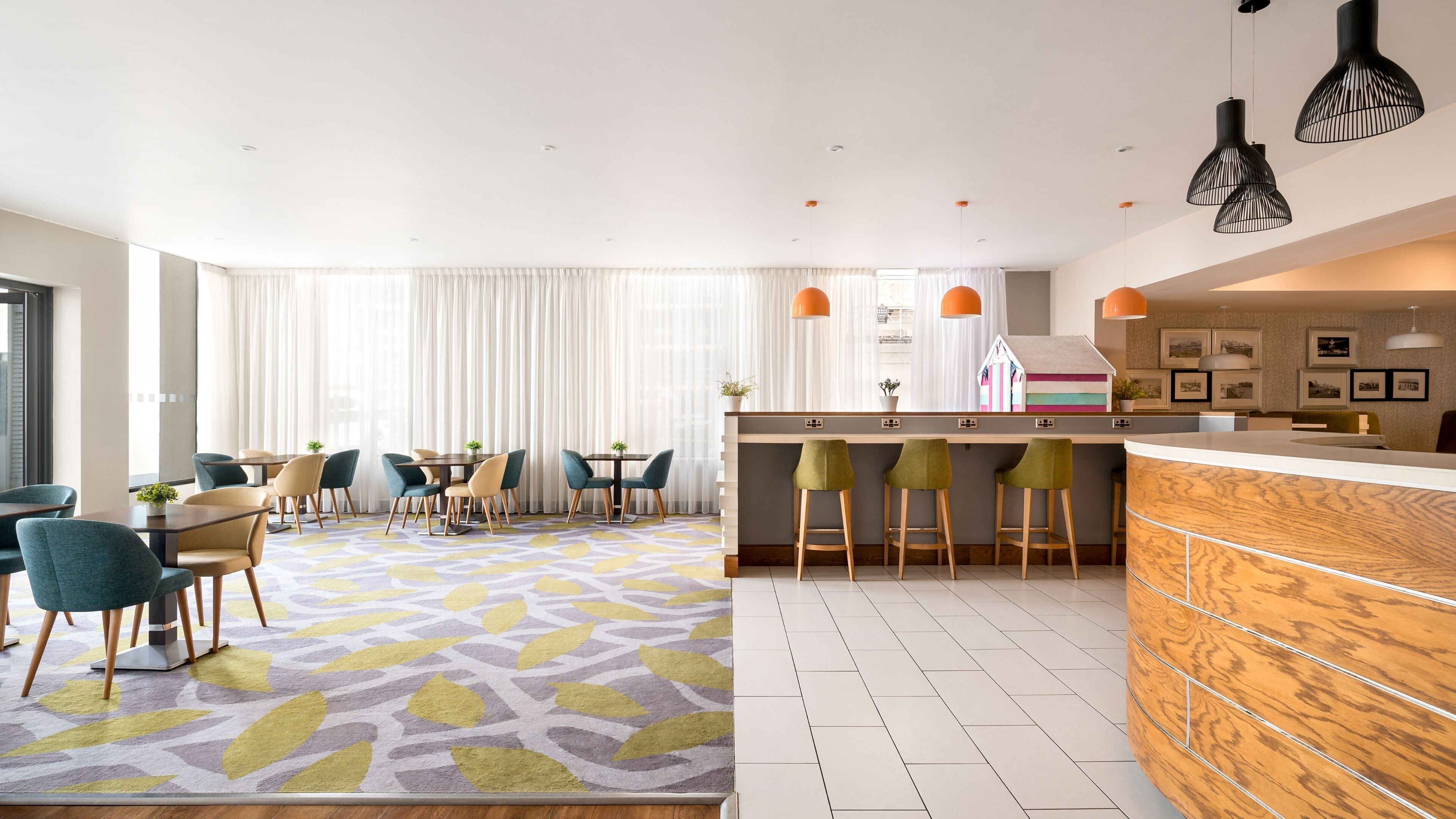 A modern hotel room with a dining area, a kitchen bar, and a living area with a patterned rug.