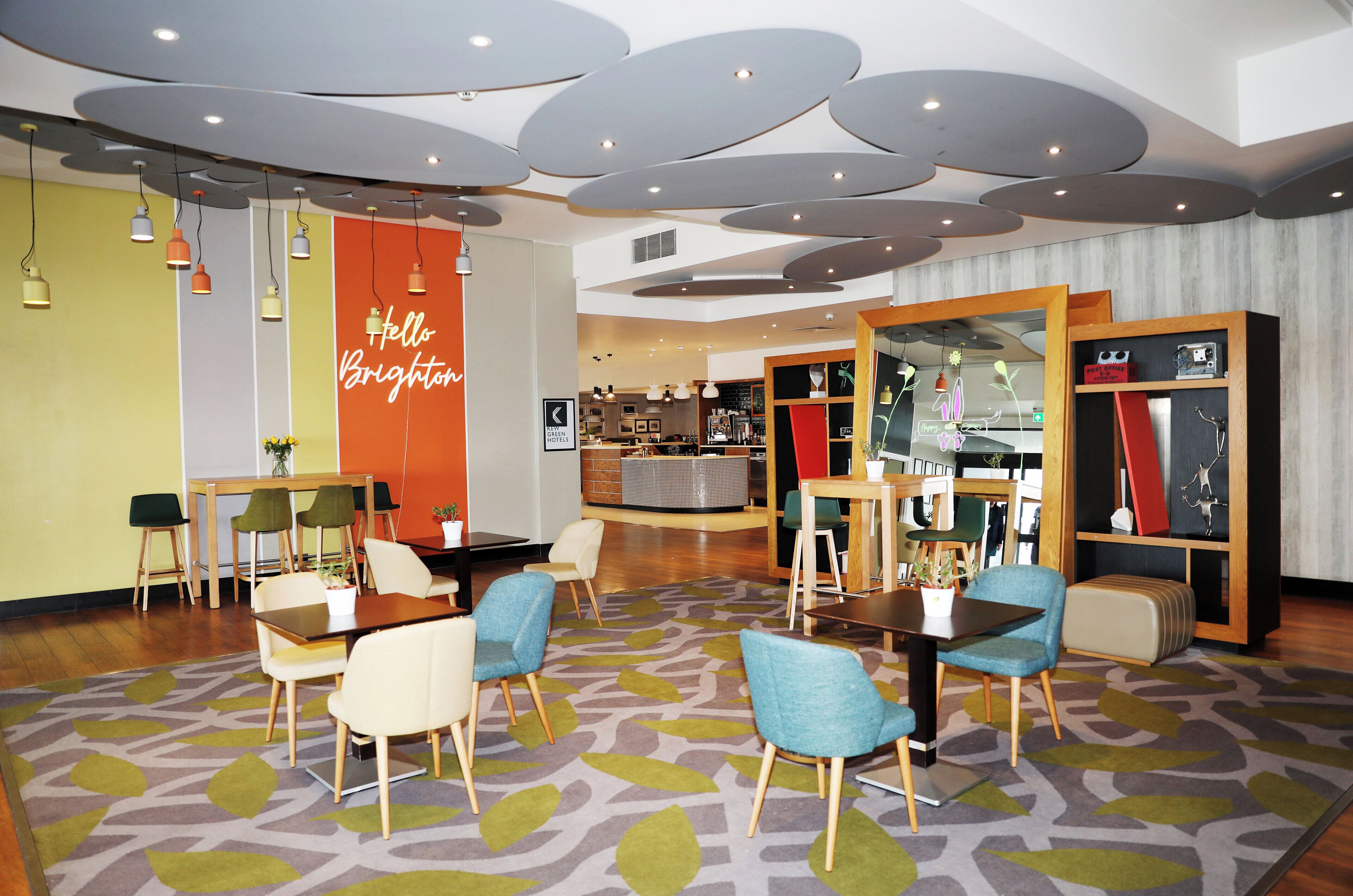 A modern hotel lobby with a central seating area, a reception desk, and a visible staircase.