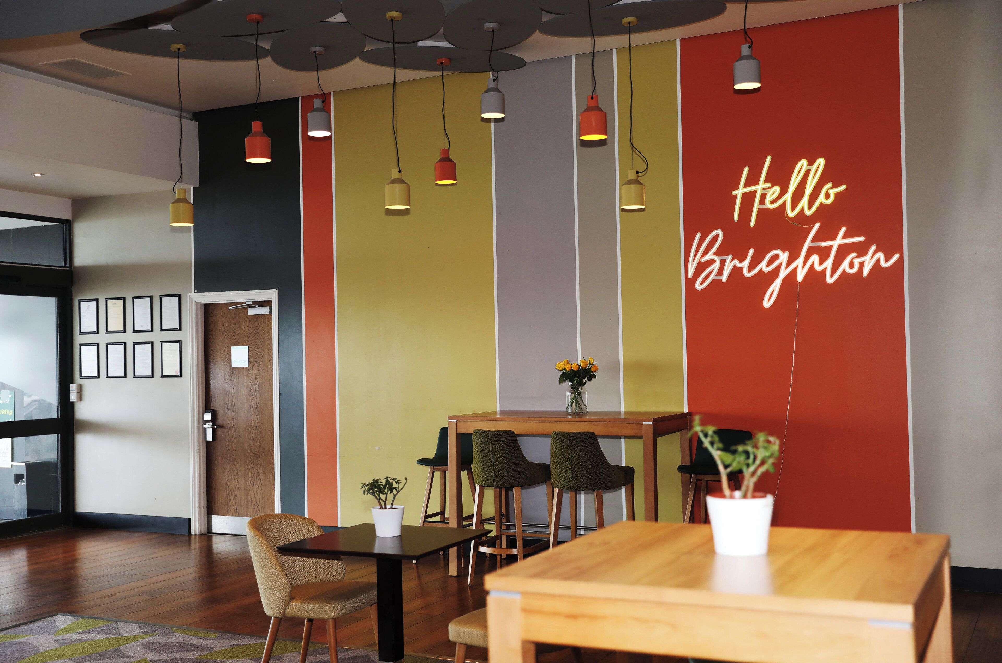 A modern interior with a wooden table, chairs, and a 'Hello Brighton' sign.