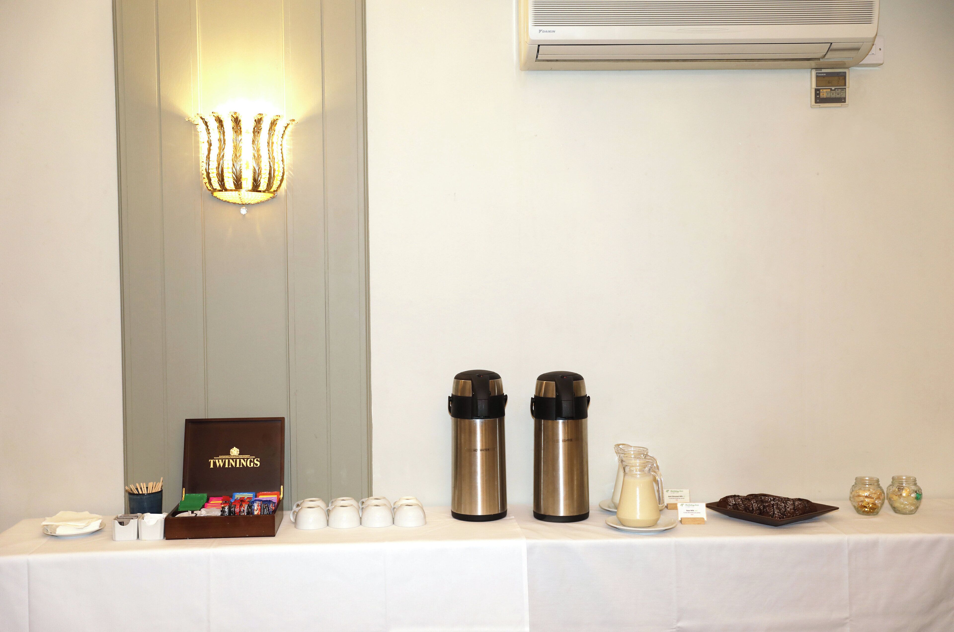 A table with a box labeled "TWININGS," two stainless steel thermos flasks, a milk jug, and two jars.