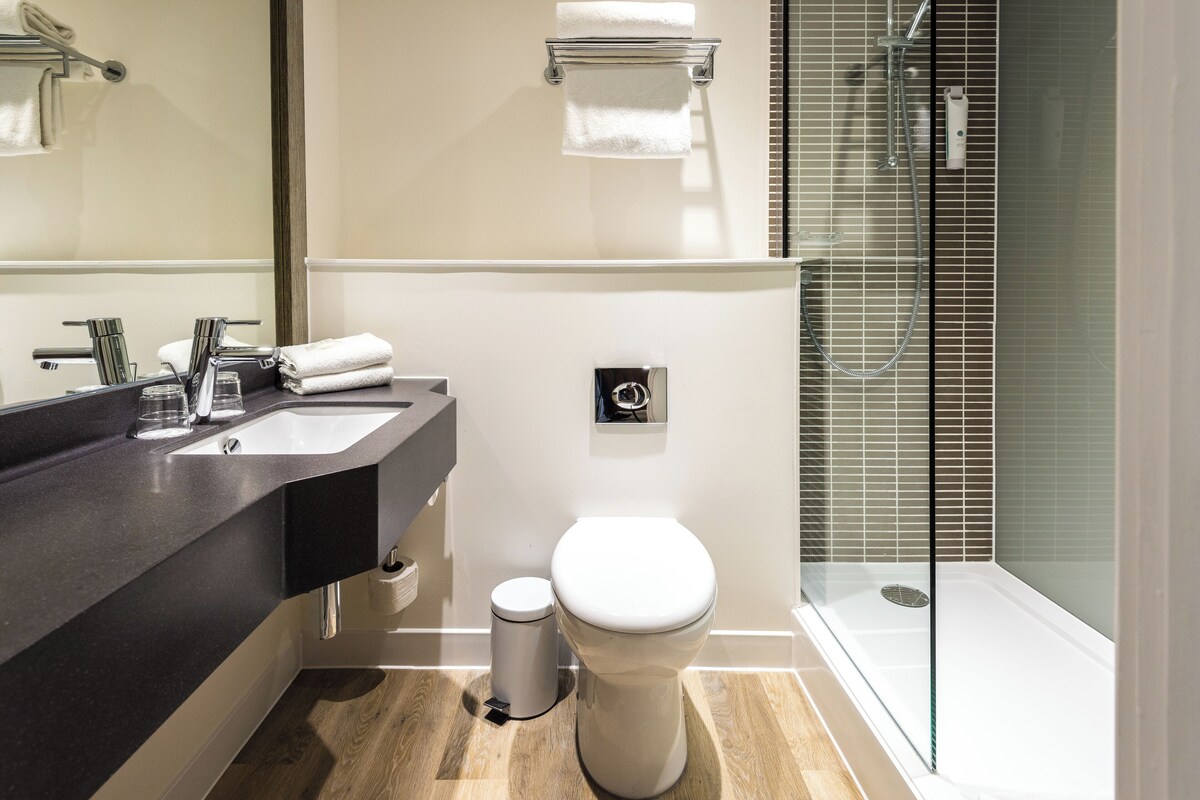 Une salle de bain moderne avec un plan de toilette foncé, des toilettes blanches et une douche à parois de verre.
