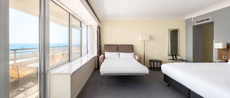 Una habitación de hotel con una cama, un escritorio, una silla, una lámpara y vista al océano.