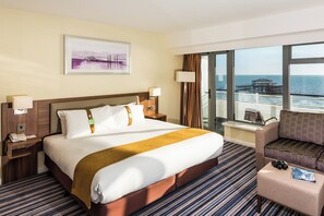 Relax in this inviting room with a large bed, nightstand, and seating area offering a view of the sea and a pier.
