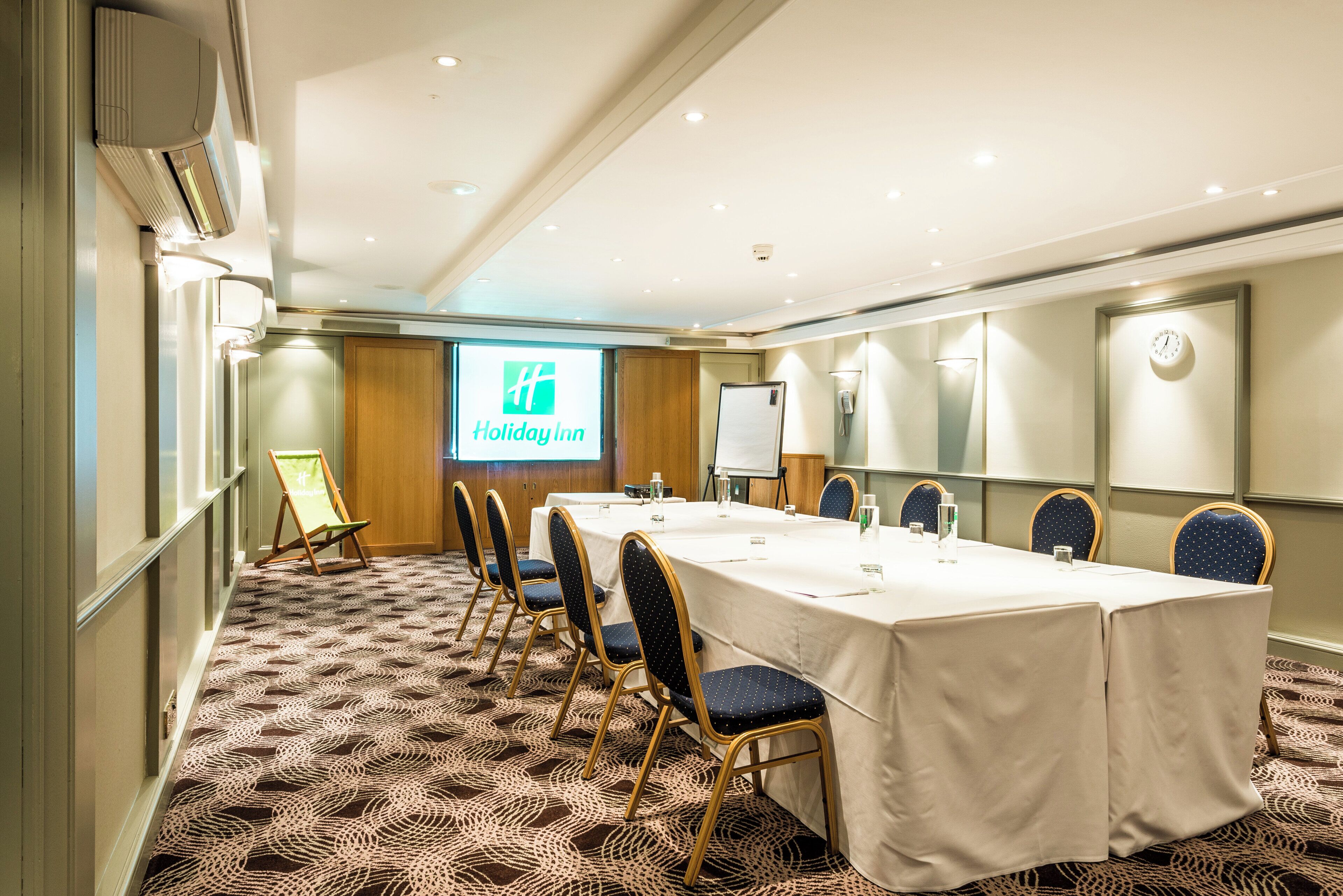 A conference room with a long table, chairs, a projector screen, and a whiteboard.