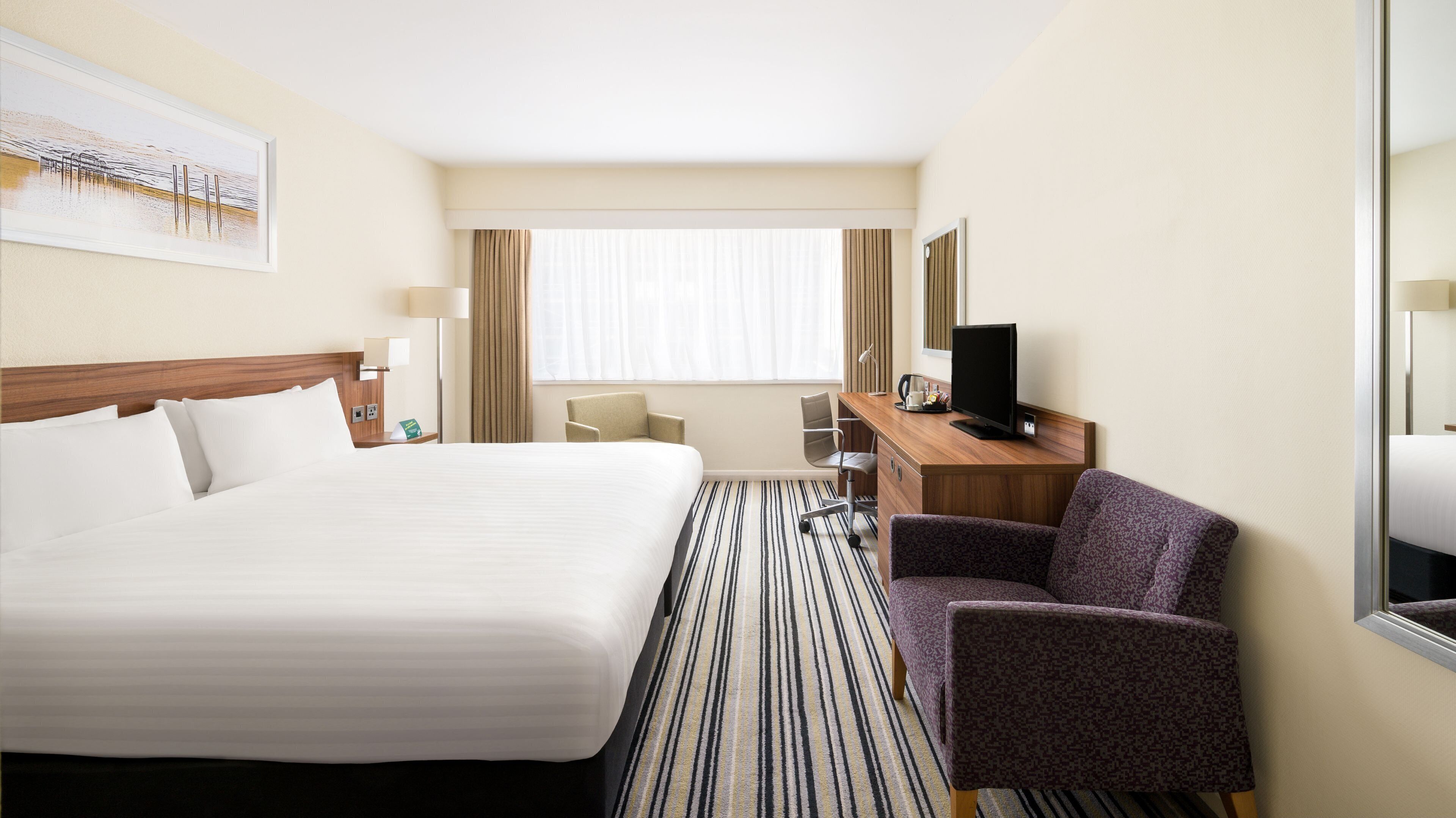 Une chambre d’hôtel avec un grand lit, un bureau avec une télévision, une chaise et une fenêtre avec des rideaux.
