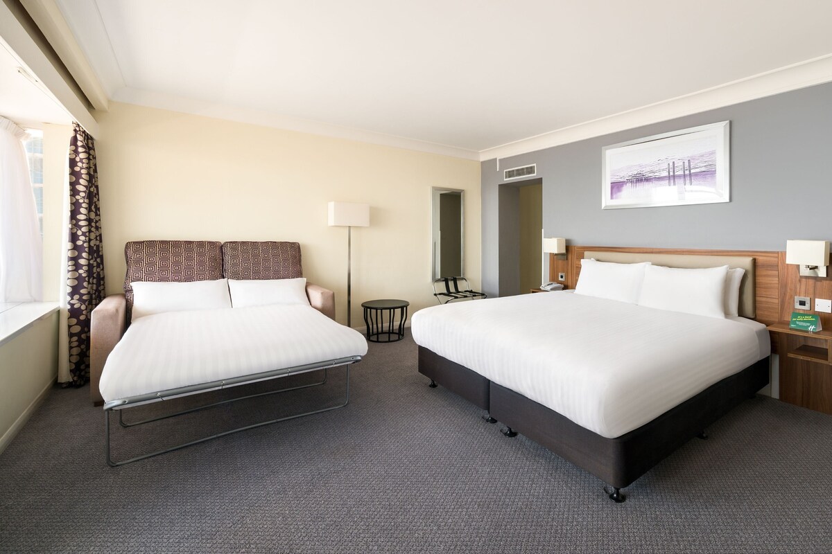 Une chambre d’hôtel avec deux lits, un bureau, une chaise, une lampe et un tableau au mur.