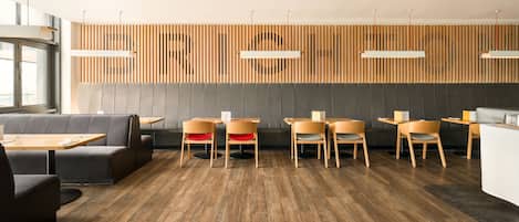 A modern restaurant interior with wooden panel walls, grey cushioned seating, and wooden tables.