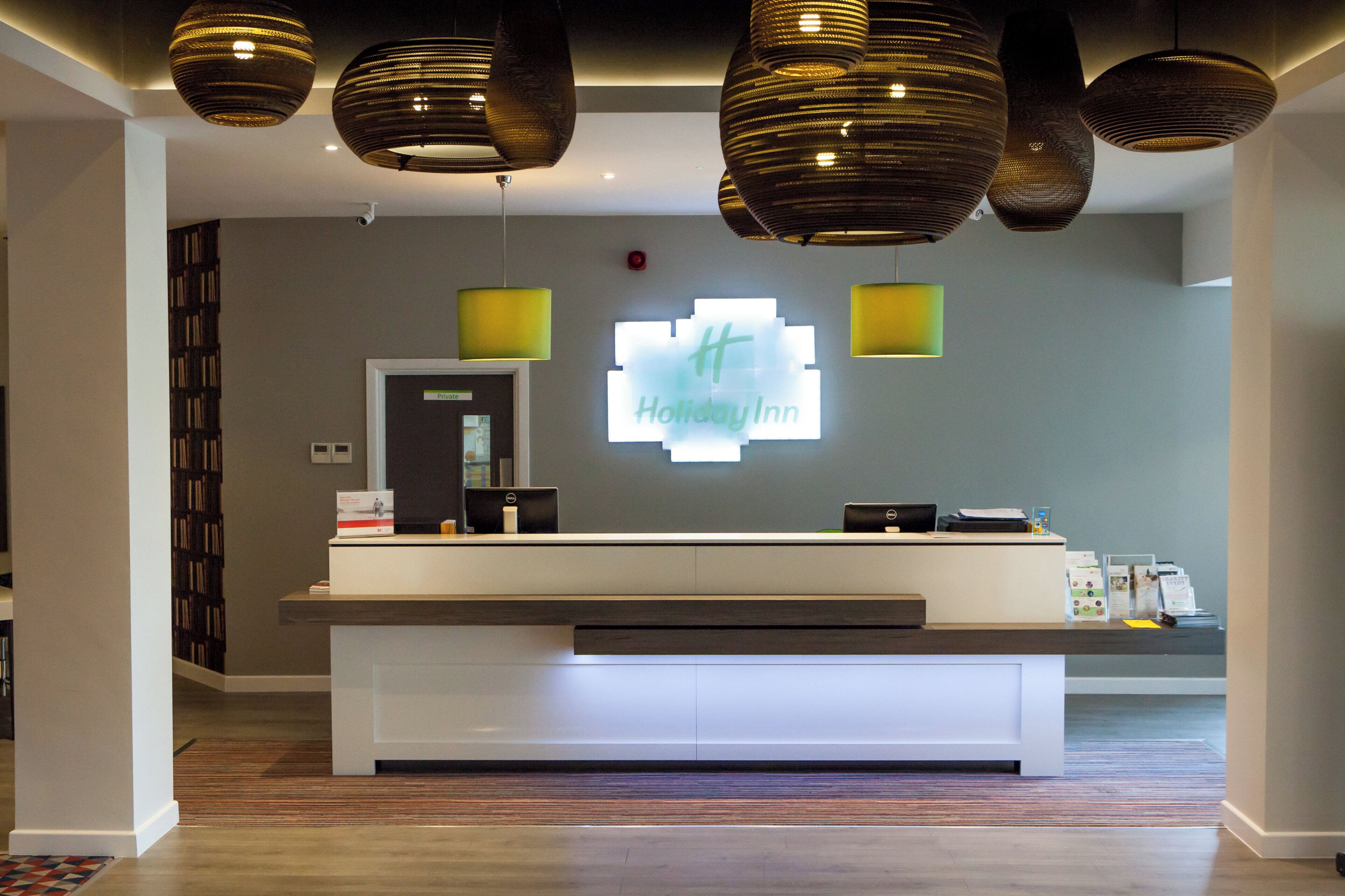 Een receptiebalie met een 'Holiday Inn' bord, een computer en een kleine plant.