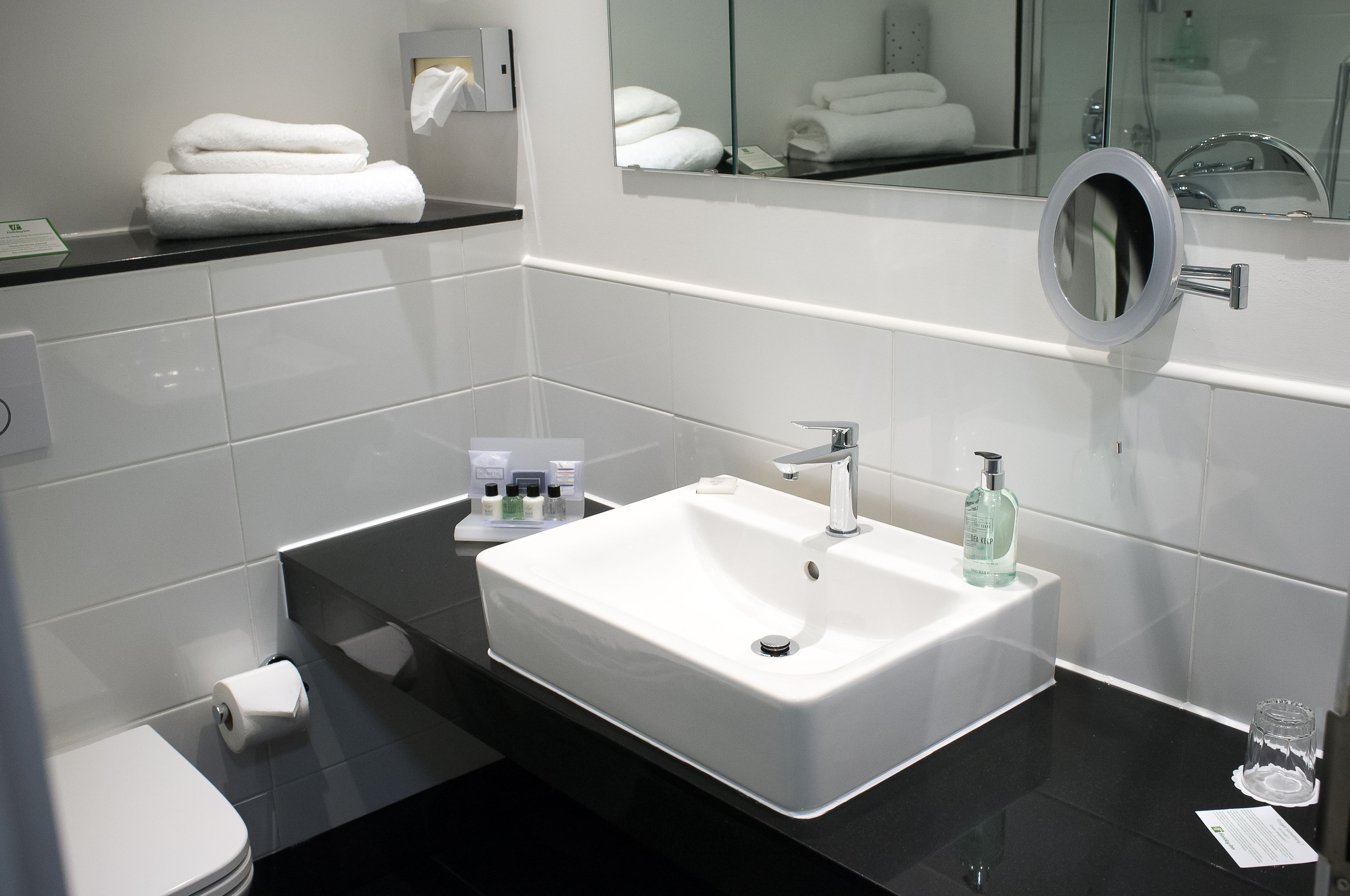 Ein modernes Badezimmer mit einem weißen Waschbecken, einer schwarzen Arbeitsplatte und einem Spiegel mit rundem Rahmen.