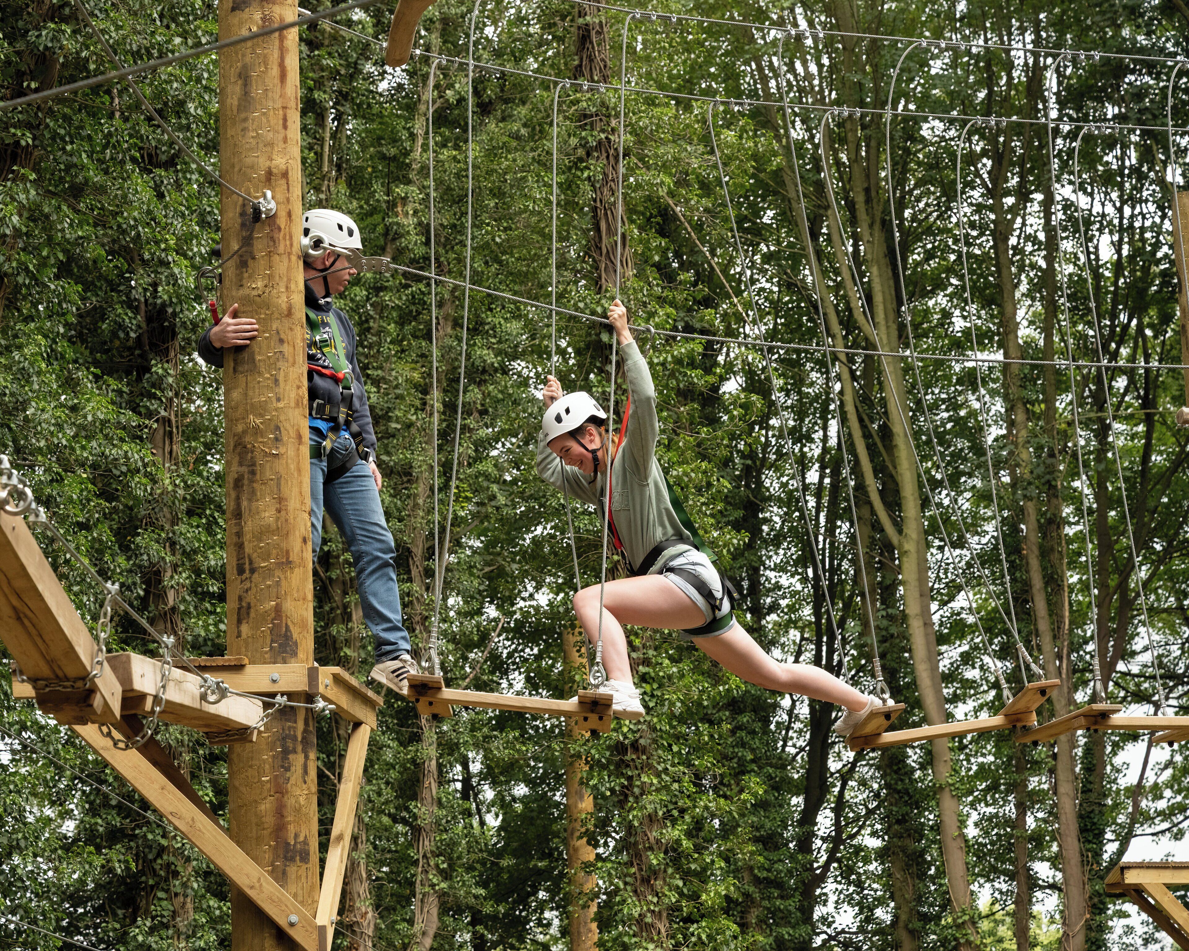 Una persona cruzando un puente colgante en un área boscosa.