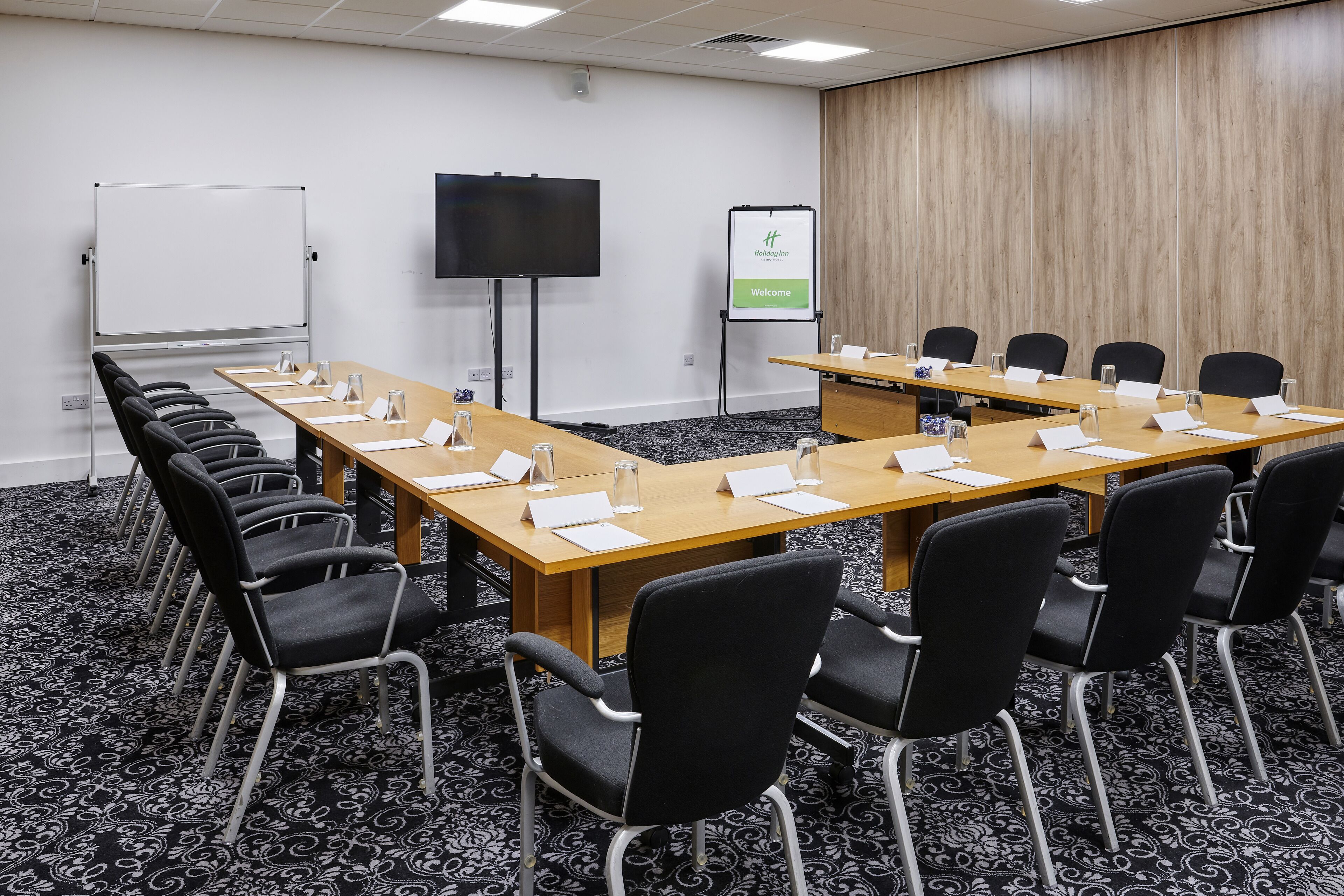 Un salón de conferencias con una larga mesa, sillas negras, una pizarra, una pantalla y un letrero de bienvenida.
