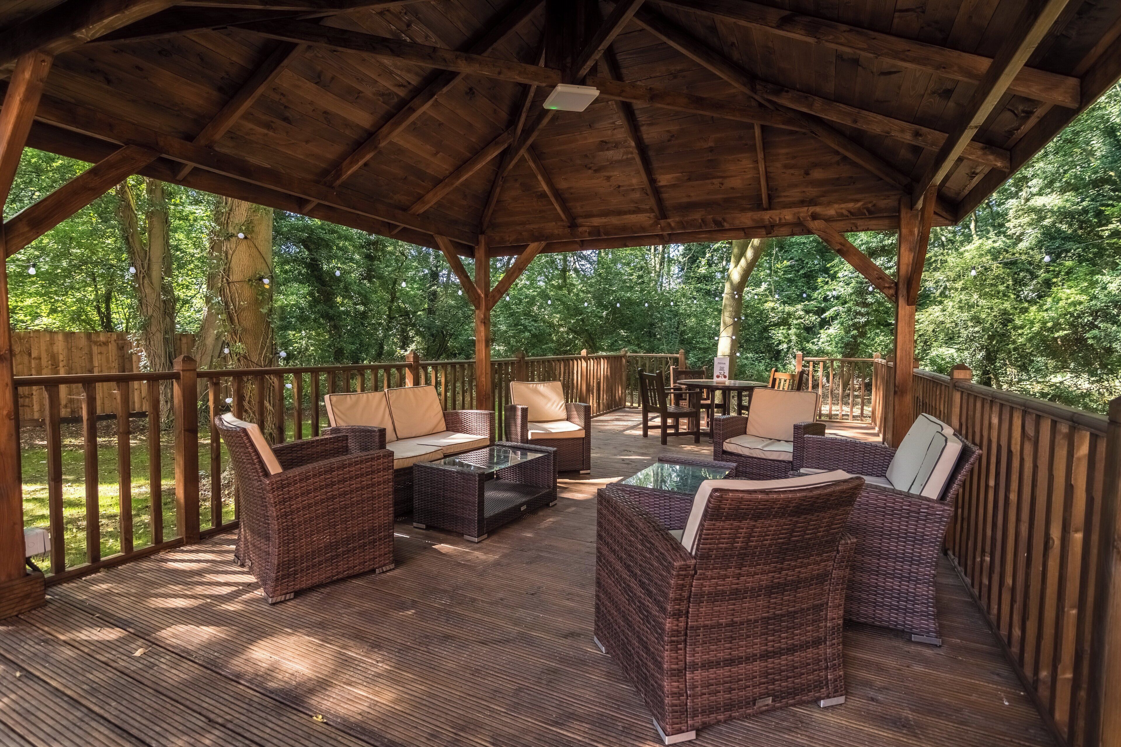 Un espacio de descanso techado al aire libre con mobiliario de mimbre y una terraza de madera.