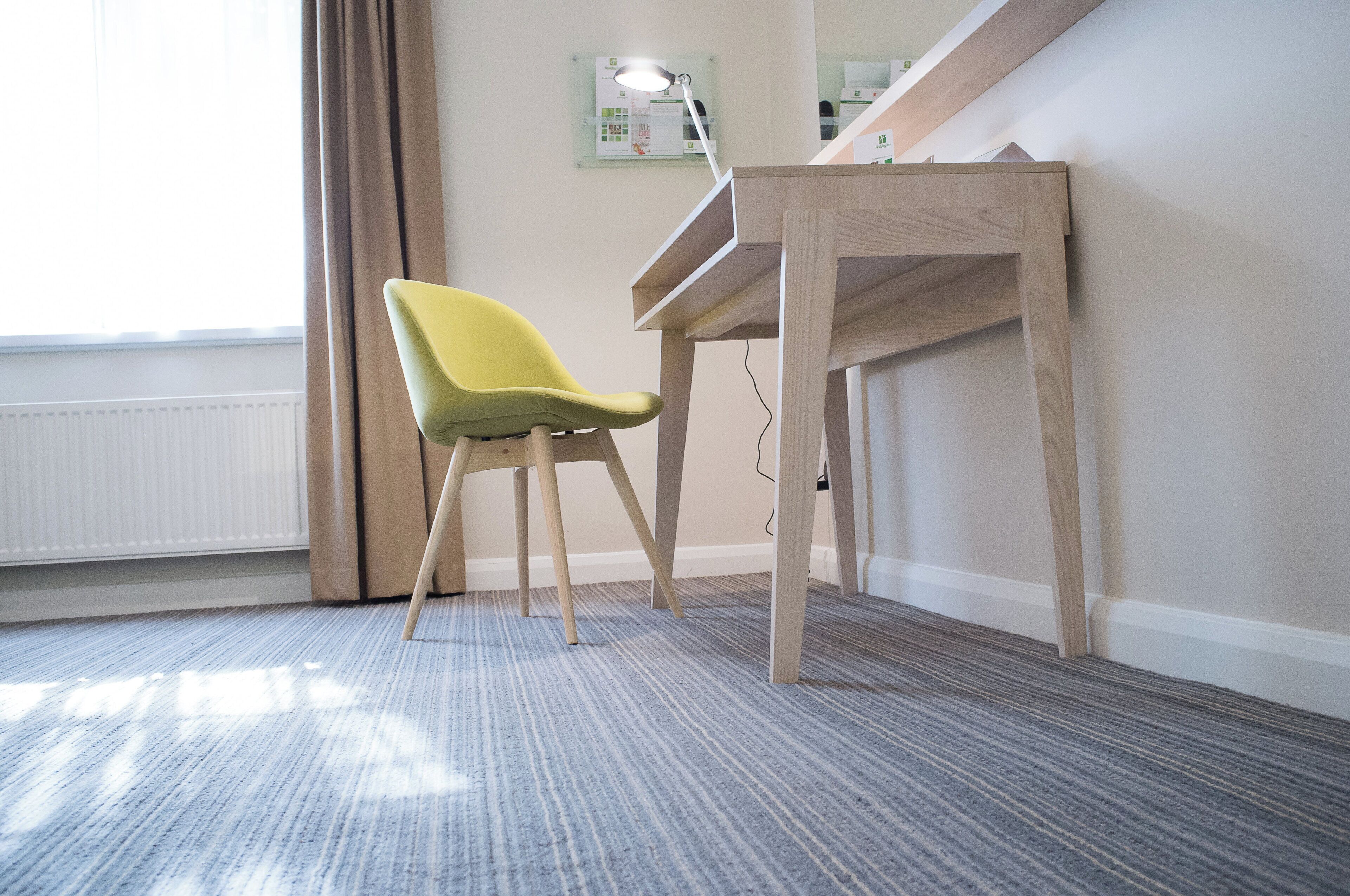 A room with a wooden desk, a yellow chair, a radiator, and a window with curtains.