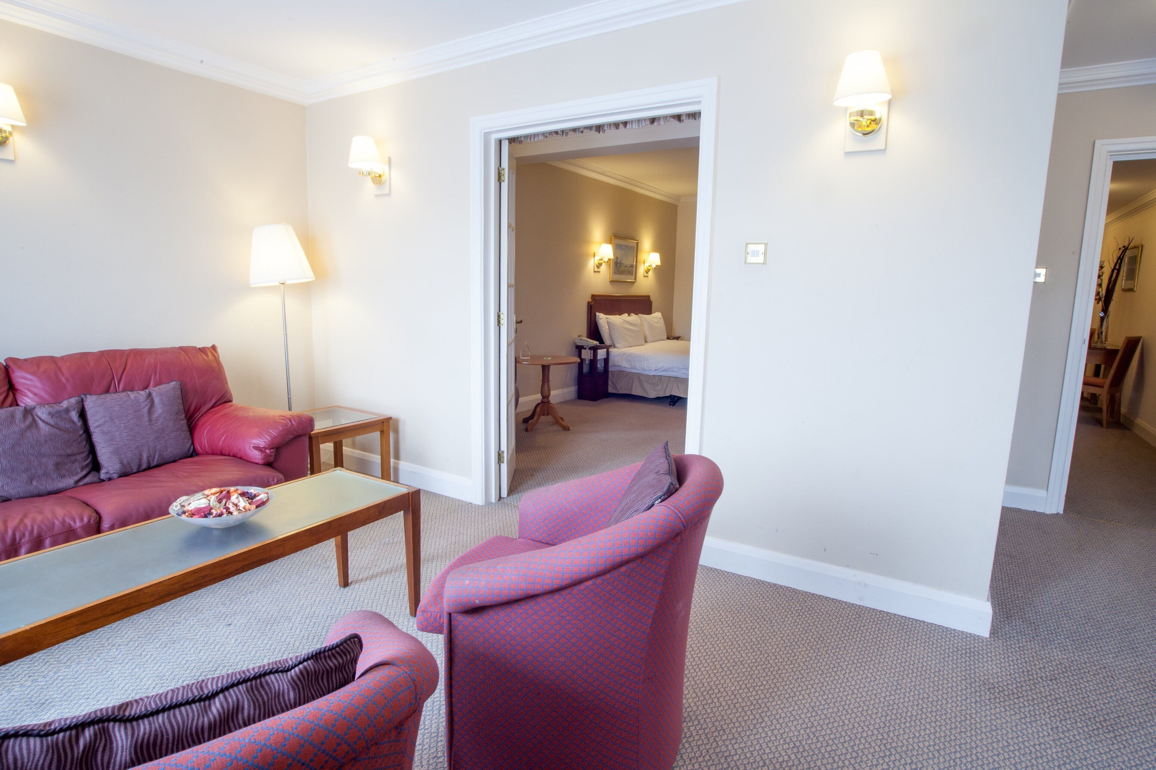 Une chambre d’hôtel avec un canapé, un fauteuil et une petite table. On y trouve un lit avec une tête de lit et deux lampes fixées au mur.