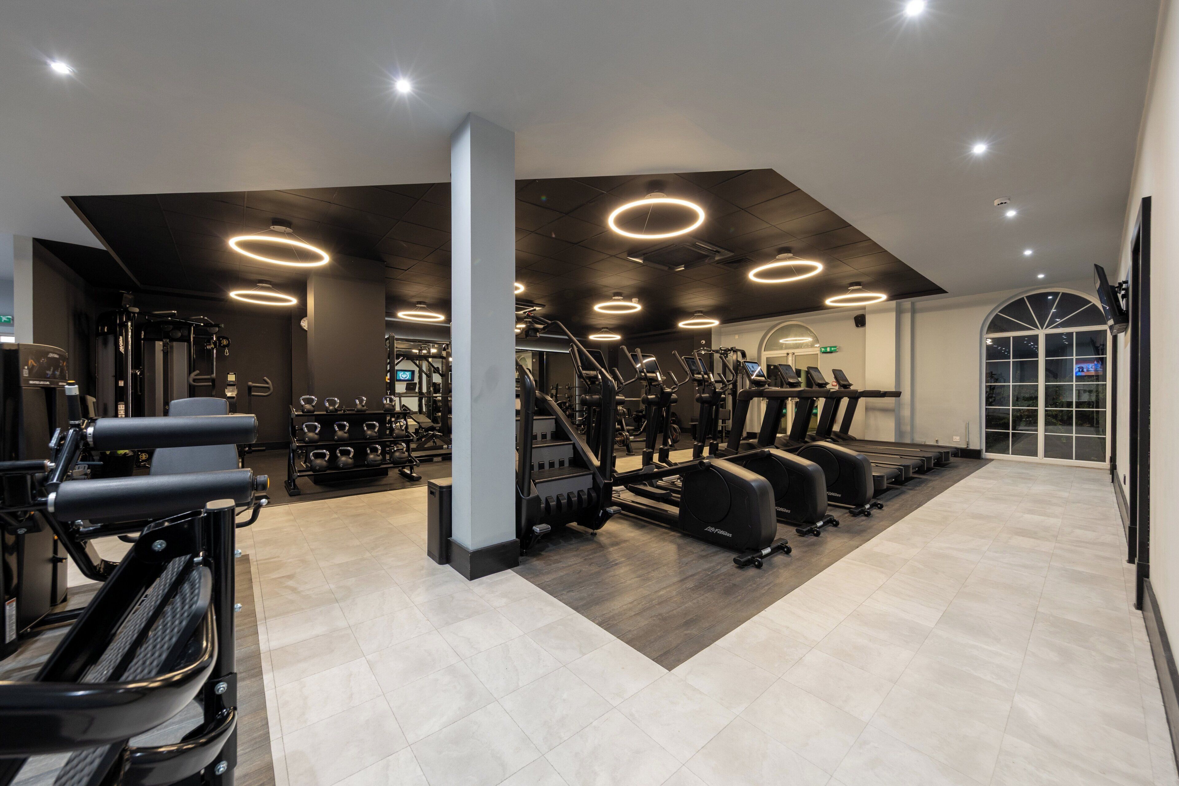 Un gimnasio moderno con diverso equipo de ejercicio, un espejo grande y una pantalla de televisión.