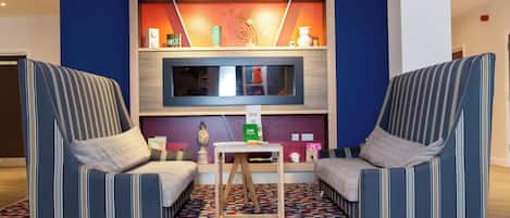 A modern lounge area with two striped armchairs, a small table, and a television mounted on a wooden panel.