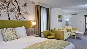 A hotel room with a large bed, two armchairs, a small table, and a nightstand with a lamp. - Holiday Inn Corby Kettering Hotel & Spa (Corby)