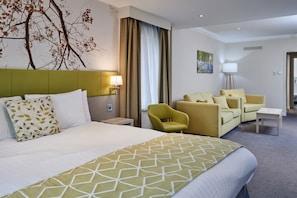 A hotel room with a large bed, two armchairs, a small table, and a nightstand with a lamp. - Holiday Inn Corby Kettering Hotel & Spa (Corby)
