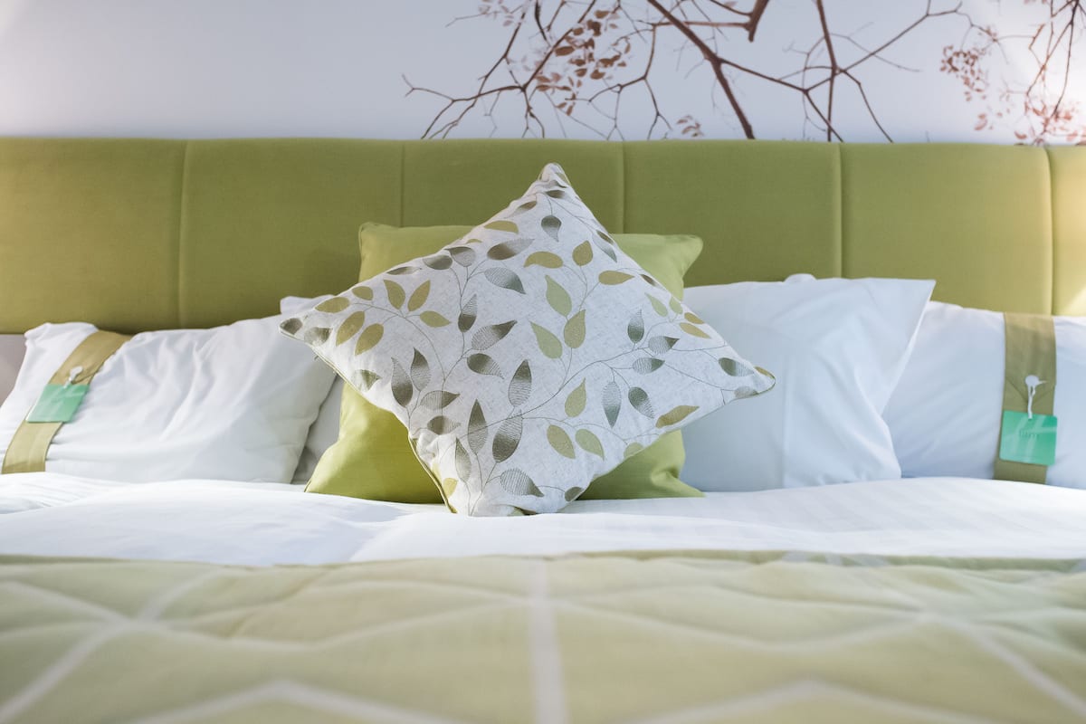 A bed with a green headboard, white and green pillows, and a white pillow with a leaf pattern.